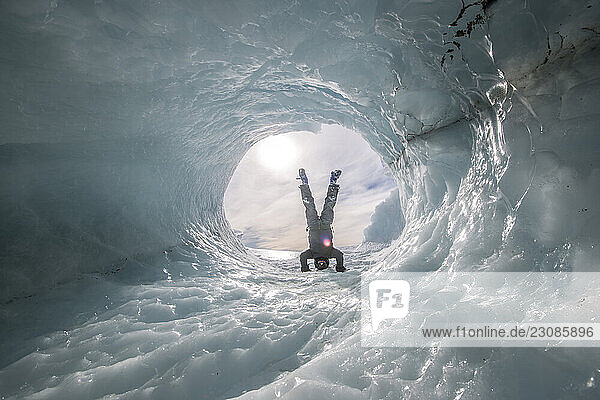 A woman stands on her head inside a tunnel through an iceberg in the Ross Sea Antarctica.