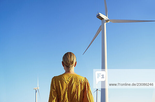 Serene contemplative woman against the clear sky and wind turbin
