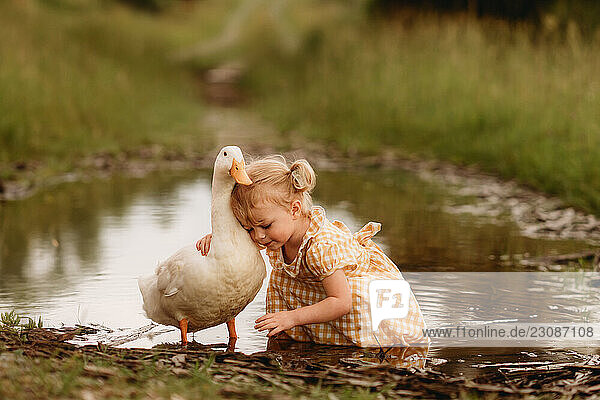 little girl in a plaid dress hugging duck in a mud puddle