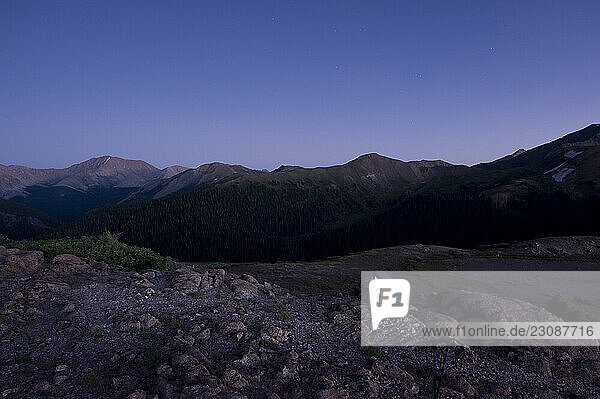 A lone TV sits among rocks in a barren field at dusk.