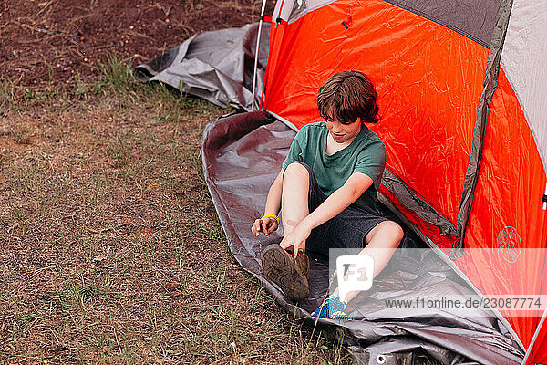Young camper putting on shoes next to tent in campground