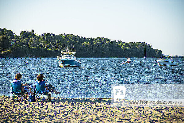 People sitting on chairs on beach with boats anchored nearby in sea