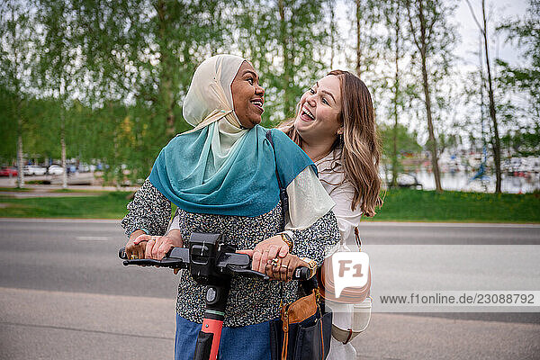 Two ethnically diverse women riding electric scooter together