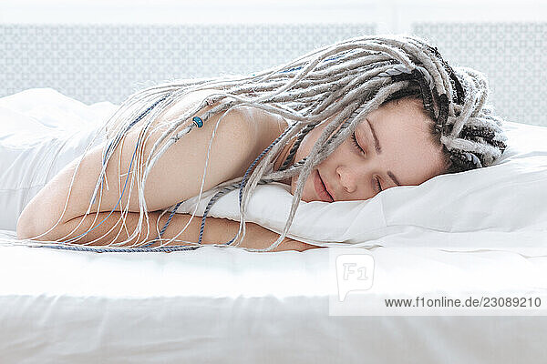 Young beautiful woman with dreadlocks sleeping in white bed.