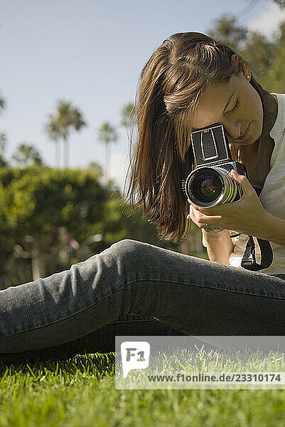 A young woman sits in grass and looks through a vintage Hasselblad camera on June 20  2009 in Beverly Hills  California.