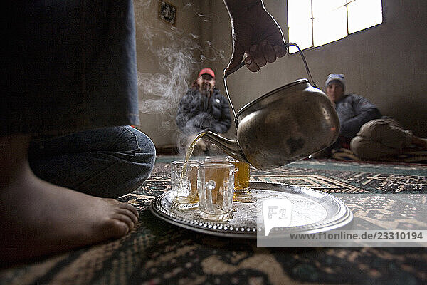 Climbers; Chris Kalous and Heidi Wirtz sit on the floor while tea is poured for them by a barefoot girl during a climbing expedition to the Wadi Rum in Jordan